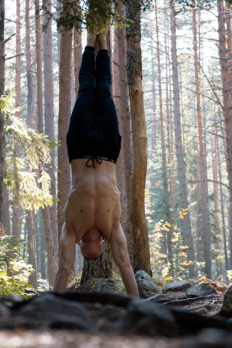 A man executes a handstand among tall trees in a serene forest environment.