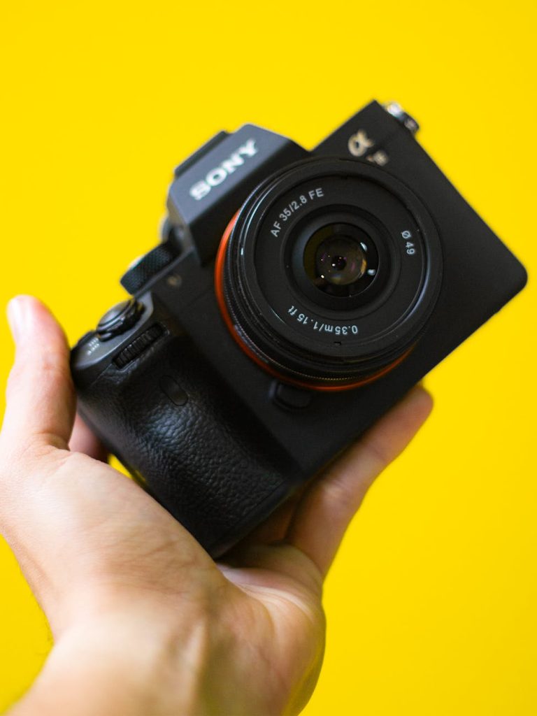 A black camera held in hand against a vibrant yellow background, showcasing its modern design.