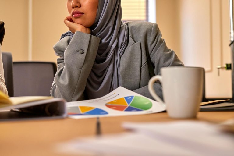 Muslim businesswoman in hijab reviewing business documents in modern office setting.
