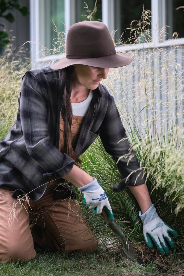 Woman wearing hat and gloves gardening in a lush green yard.