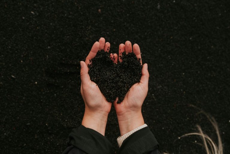A close-up of hands holding black sand in a heart shape, symbolizing care for nature.