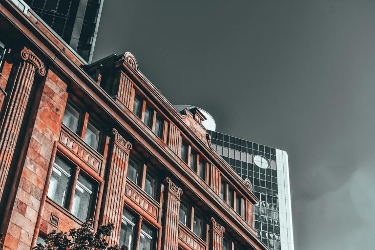 Low angle of modern multistory office next to old historical building under gloomy overcast sky in daytime