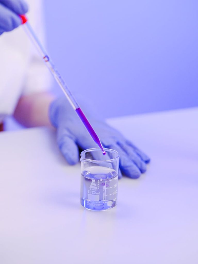 Close-up of a gloved hand pipetting liquid into a beaker in a lab.